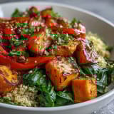 A fully assembled warm salad bowl with wholesome grains, vibrant roasted vegetables, and greens, topped with crumbled feta, pumpkin seeds, and fresh herbs.