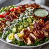 Freshly prepared Cobb Salad Bowl featuring colorful rows of chicken, bacon, tomatoes, and avocado over crisp greens, served with dressing on the side.