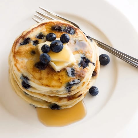 Fluffy blueberry pancakes, golden and piled high, drizzled with sweet maple syrup and melted butter.
