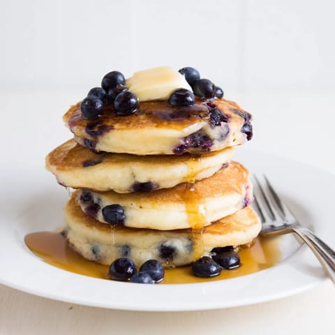 American breakfast of warm blueberry pancakes, studded with juicy blueberries, ready to eat alongside syrup.