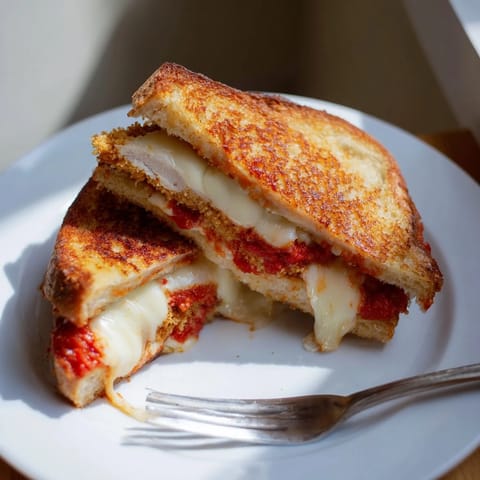 Golden, crispy Chicken Parm Grilled Cheese with melted mozzarella and warm marinara, served on garlic-buttered sourdough slices.  
