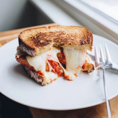 A close-up of Chicken Parm Grilled Cheese, featuring fried chicken cutlets and zesty marinara tucked between buttery, golden bread.  