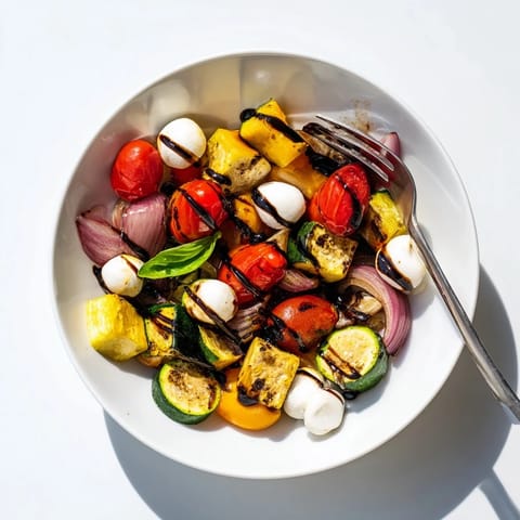 Warm, caramelized vegetables and creamy mozzarella pearls create a colorful, vegetarian Roasted Veggie Caprese Salad served with a sweet-tangy balsamic drizzle.