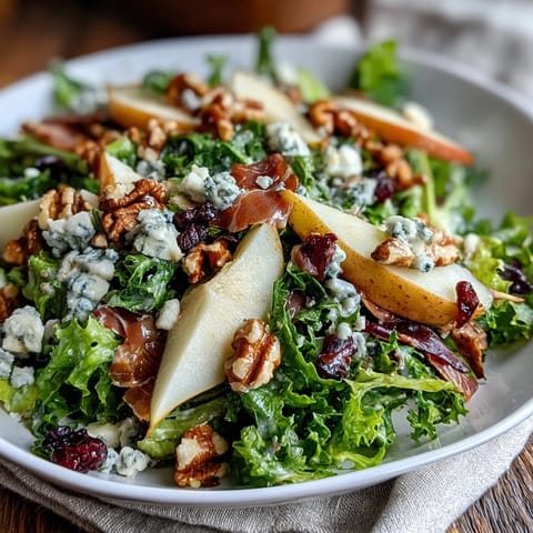 Fresh frisée lettuce, sliced ripe pears, and crumbled blue cheese topped with crispy prosciutto pieces in a salad bowl.