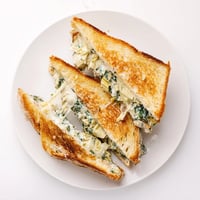 Golden-brown sourdough grilled cheese filled with creamy spinach and artichoke dip, served warm.  