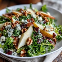 Fresh frisée lettuce, sliced ripe pears, and crumbled blue cheese topped with crispy prosciutto pieces in a salad bowl.